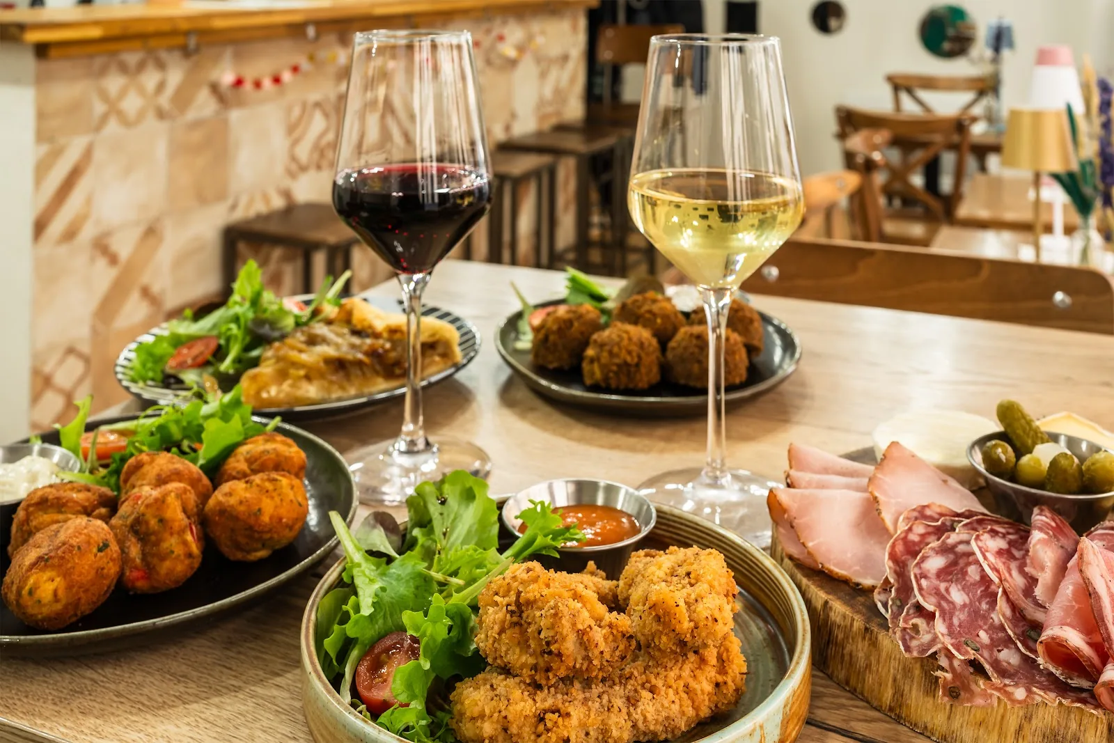 Un verre de rouge et un verre de blanc sur une table de L'Œno'Vice, avec charcuterie, fromages et croquettes
